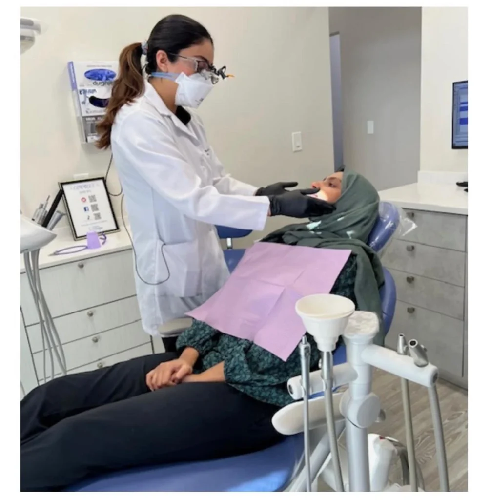 Dr. Zoha Abid, in loupes and a protective mask, examining a patient in the dental chair